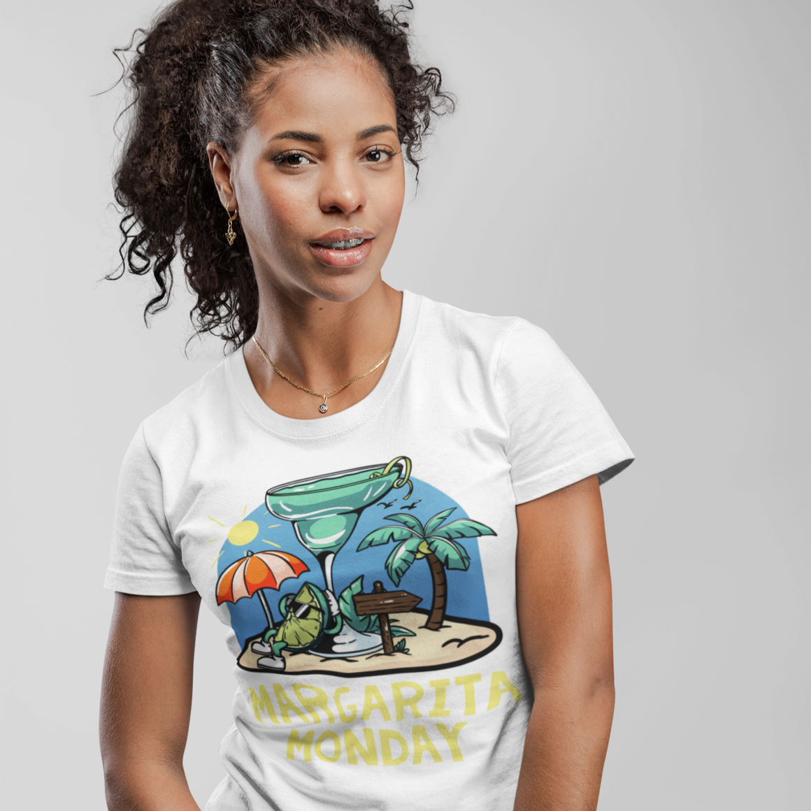 Margarita Monday T-shirt Design Ideas featuring a white t-shirt with a colorful tropical design of a margarita glass, palm trees, a sun umbrella, and a sandy beach scene, complemented by bold yellow text reading 'Margarita Monday.' Modeled by a woman with a cheerful and casual vibe