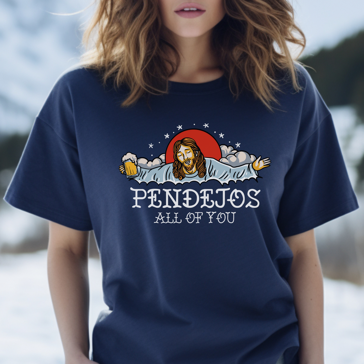 A person wearing a red t-shirt featuring an illustration of a bearded figure with open arms, holding a beer mug, surrounded by clouds and a red sun. The text "PENDEJOS ALL OF YOU" is printed below the image.