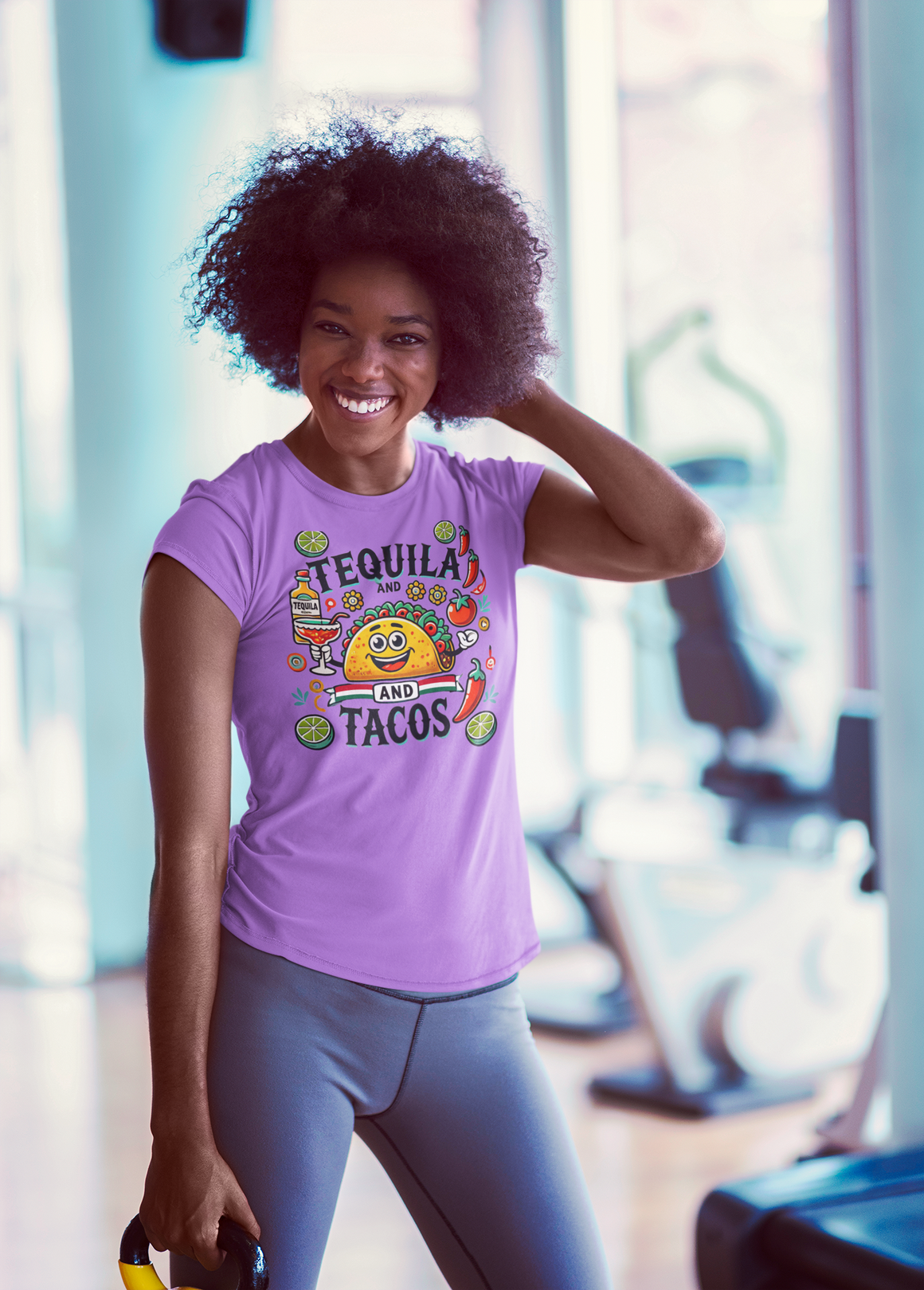 Purple t-shirt featuring a festive 'Tequila and Tacos' design with a smiling taco character, tequila bottle, margarita glass, lime slices, and chili peppers. Perfect for celebrating fiestas and taco nights with a fun and lively style.