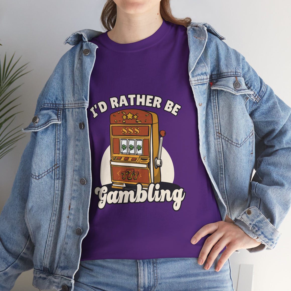 Person wearing a purple t-shirt with the text "I'd Rather Be Gambling" and an illustration of a slot machine. This funny casino game shirt is perfect for anyone who loves gambling humor and casino-inspired designs