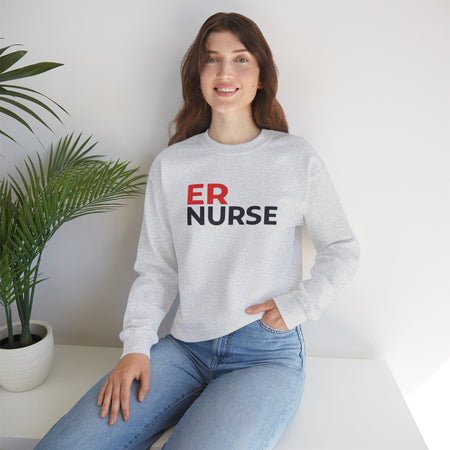 A woman smiling and wearing a light gray ER Nurse Sweatshirt, sitting casually with a potted plant beside her.