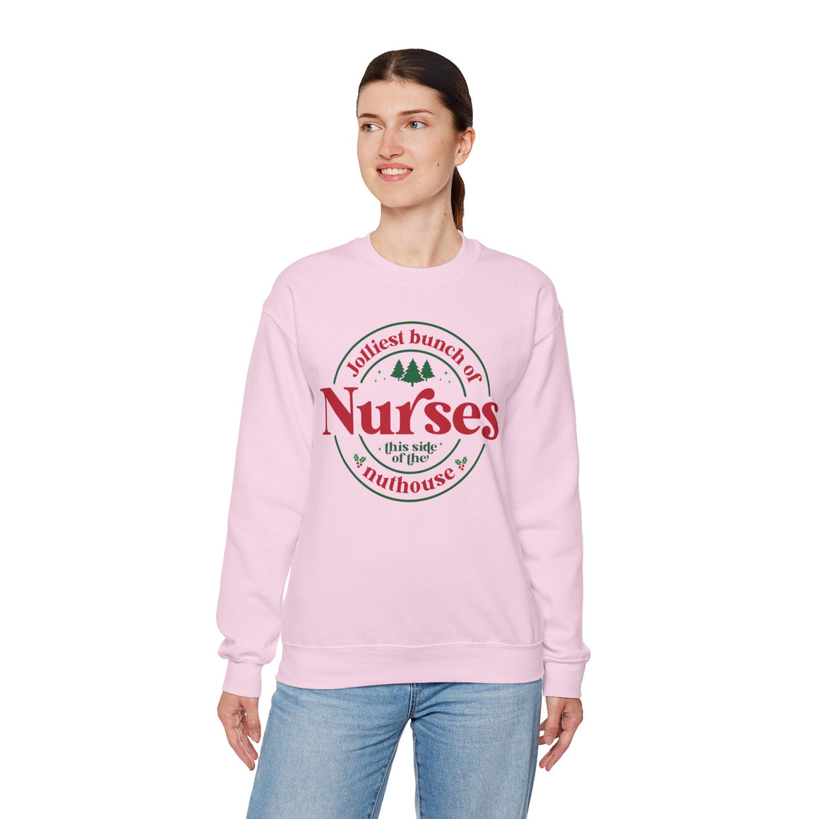 Pink Christmas sweatshirt with the humorous phrase 'Jolliest bunch of Nurses this side of the nuthouse,' surrounded by festive elements like trees and holly. A perfect holiday-themed gift for nurses with a sense of humor, celebrating Christmas in a fun and lighthearted style.