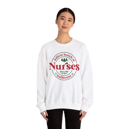 White Christmas sweatshirt with the humorous phrase 'Jolliest bunch of Nurses this side of the nuthouse,' surrounded by festive elements like trees and holly. A perfect holiday-themed gift for nurses with a sense of humor, celebrating Christmas in a fun and lighthearted style.