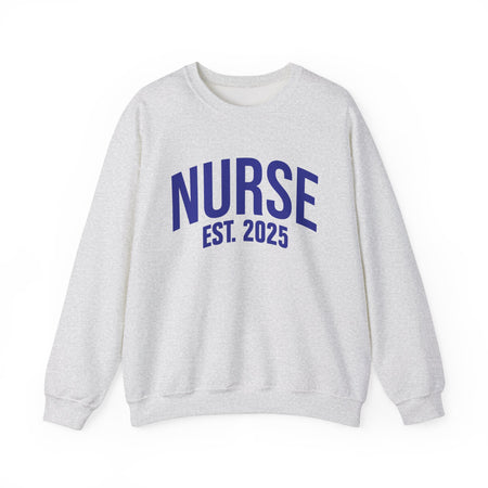 A white sweatshirt with bold blue text reading "NURSE EST. 2025." He stands confidently against a plain white background, smiling slightly. The sweatshirt design highlights the keyphrase "Nurse Est. 2025," making it a stylish and comfortable option for nursing students, graduates, or future nurses.