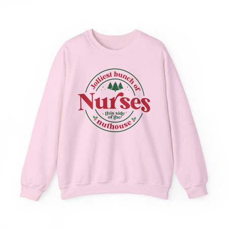 Pink Christmas sweatshirt with the humorous phrase 'Jolliest bunch of Nurses this side of the nuthouse,' surrounded by festive elements like trees and holly. A perfect holiday-themed gift for nurses with a sense of humor, celebrating Christmas in a fun and lighthearted style.