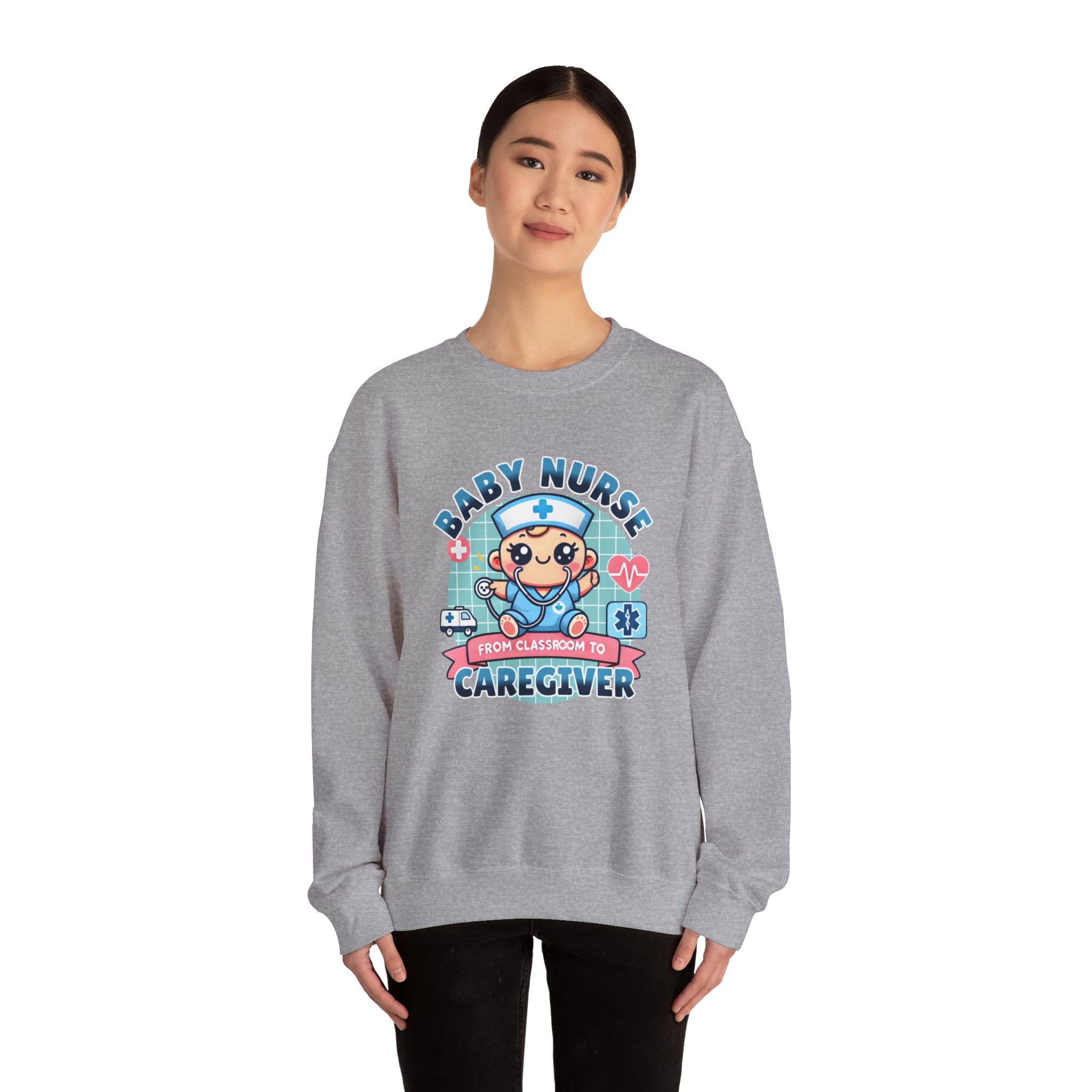 Woman wearing a Slate Grey sweatshirt with a cute, cartoon-style design that reads 'Baby Nurse - From Classroom to Caregiver.' The graphic features a smiling baby nurse character in scrubs, holding a stethoscope, with icons of medical elements like an ambulance, heartbeat, and medical cross around. 