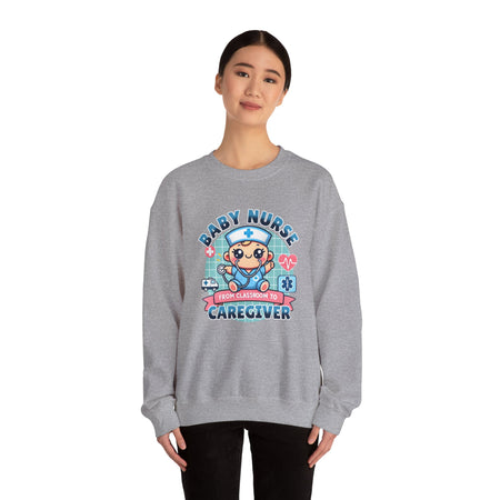 Woman wearing a Slate Grey sweatshirt with a cute, cartoon-style design that reads 'Baby Nurse - From Classroom to Caregiver.' The graphic features a smiling baby nurse character in scrubs, holding a stethoscope, with icons of medical elements like an ambulance, heartbeat, and medical cross around. 