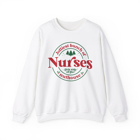 White Christmas sweatshirt with the humorous phrase 'Jolliest bunch of Nurses this side of the nuthouse,' surrounded by festive elements like trees and holly. A perfect holiday-themed gift for nurses with a sense of humor, celebrating Christmas in a fun and lighthearted style.