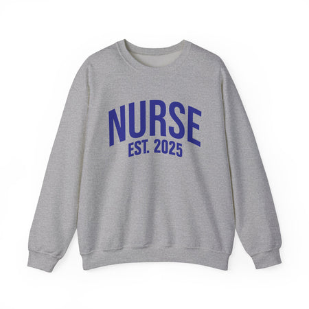 A light grey sweatshirt with bold blue text reading "NURSE EST. 2025." He stands confidently against a plain white background, smiling slightly. The sweatshirt design highlights the keyphrase "Nurse Est. 2025," making it a stylish and comfortable option for nursing students, graduates, or future nurses.