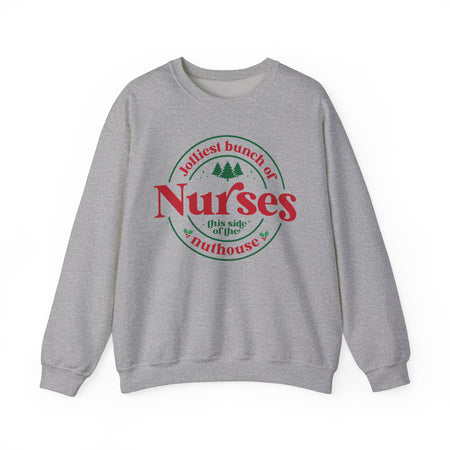 Grey Christmas sweatshirt with the humorous phrase 'Jolliest bunch of Nurses this side of the nuthouse,' surrounded by festive elements like trees and holly. A perfect holiday-themed gift for nurses with a sense of humor, celebrating Christmas in a fun and lighthearted style.