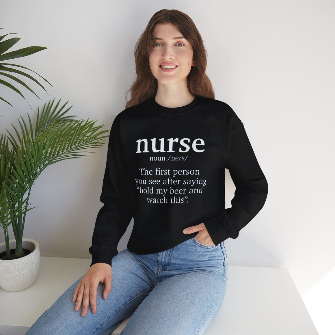 Woman wearing a black sweatshirt with the humorous text 'nurse: The first person you see after saying hold my beer and watch this.' Ideal for those looking for funny nurse-themed shirts that add a touch of humor to their wardrobe.