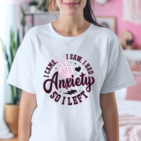 A woman wearing a white T-shirt with a playful design that reads "I Came. I Saw. I Had Anxiety So I Left," featuring a skeleton hand making a peace sign. This Funny Anxiety T-shirt humorously expresses the sentiment with bold, creative lettering and symbols.