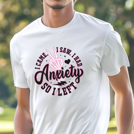 A man wearing a white T-shirt with the humorous design "I Came. I Saw. I Had Anxiety So I Left," featuring a skeleton hand making a peace sign. This Funny Anxiety T-shirt playfully captures the sentiment with bold, stylish lettering and icons.