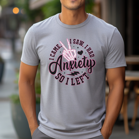 A man wearing a gray T-shirt with the humorous phrase "I Came. I Saw. I Had Anxiety So I Left," featuring a skeleton hand making a peace sign. This Funny Anxiety T-shirt creatively conveys the sentiment with bold, playful lettering and symbols.