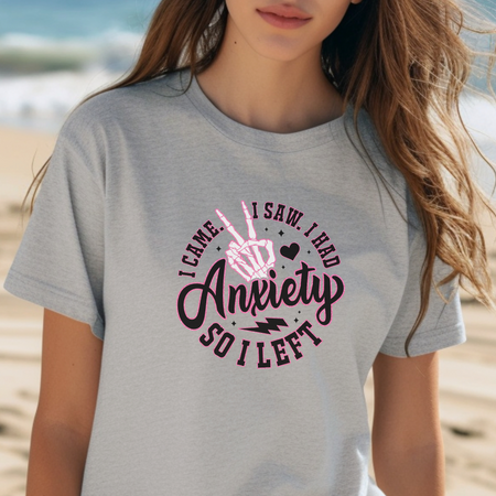 A woman wearing a gray T-shirt with the playful phrase "I Came. I Saw. I Had Anxiety So I Left," featuring a skeleton hand making a peace sign. This Funny Anxiety T-shirt humorously captures the sentiment with bold, creative lettering and symbols.