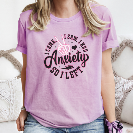 A woman wearing a lavender T-shirt with the humorous phrase "I Came. I Saw. I Had Anxiety So I Left," featuring a skeleton hand making a peace sign. This Funny Anxiety T-shirt creatively expresses the sentiment with bold, playful lettering and symbols.
