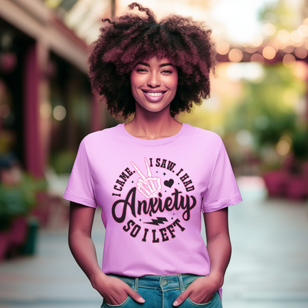 Text: A woman wearing a pink T-shirt with the playful phrase "I Came. I Saw. I Had Anxiety So I Left," featuring a skeleton hand making a peace sign. This Funny Anxiety T-shirt humorously conveys the sentiment with bold, creative lettering and symbols.