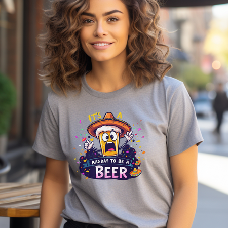 Woman wearing a gray Fiesta San Antonio T-shirt featuring a cartoon beer character in a sombrero, surrounded by colorful confetti. The text reads 'It's a bad day to be a beer.