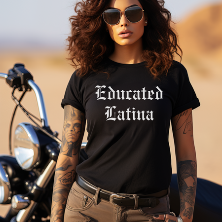 Confident woman with sunglasses and tattoos standing next to a motorcycle in the desert, wearing a black t-shirt with 'Educated Latina' in bold old English font. This shirt represents educated Latina T-shirt sayings and quotes, celebrating Latina pride, strength, and cultural identity. Perfect for those who embrace their heritage with a bold and stylish look.