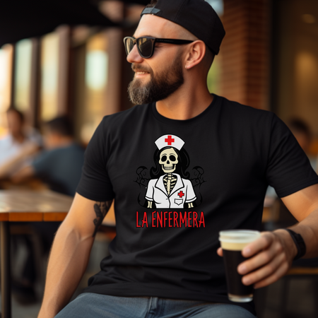 Man wearing a "La Enfermera Loteria Shirt" featuring a skeleton nurse in a white uniform with a red cross on the cap and chest, holding a drink outdoors. The design resembles a loteria card with "La Enfermera" in bold red letters, capturing a Día de los Muertos and healthcare theme.