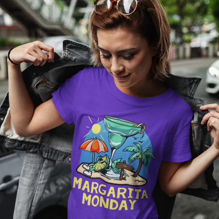 A woman wearing a purple t-shirt with a fun "Margarita Monday" design, showcasing tropical vibes with a large margarita glass, palm trees, and a beach scene. 