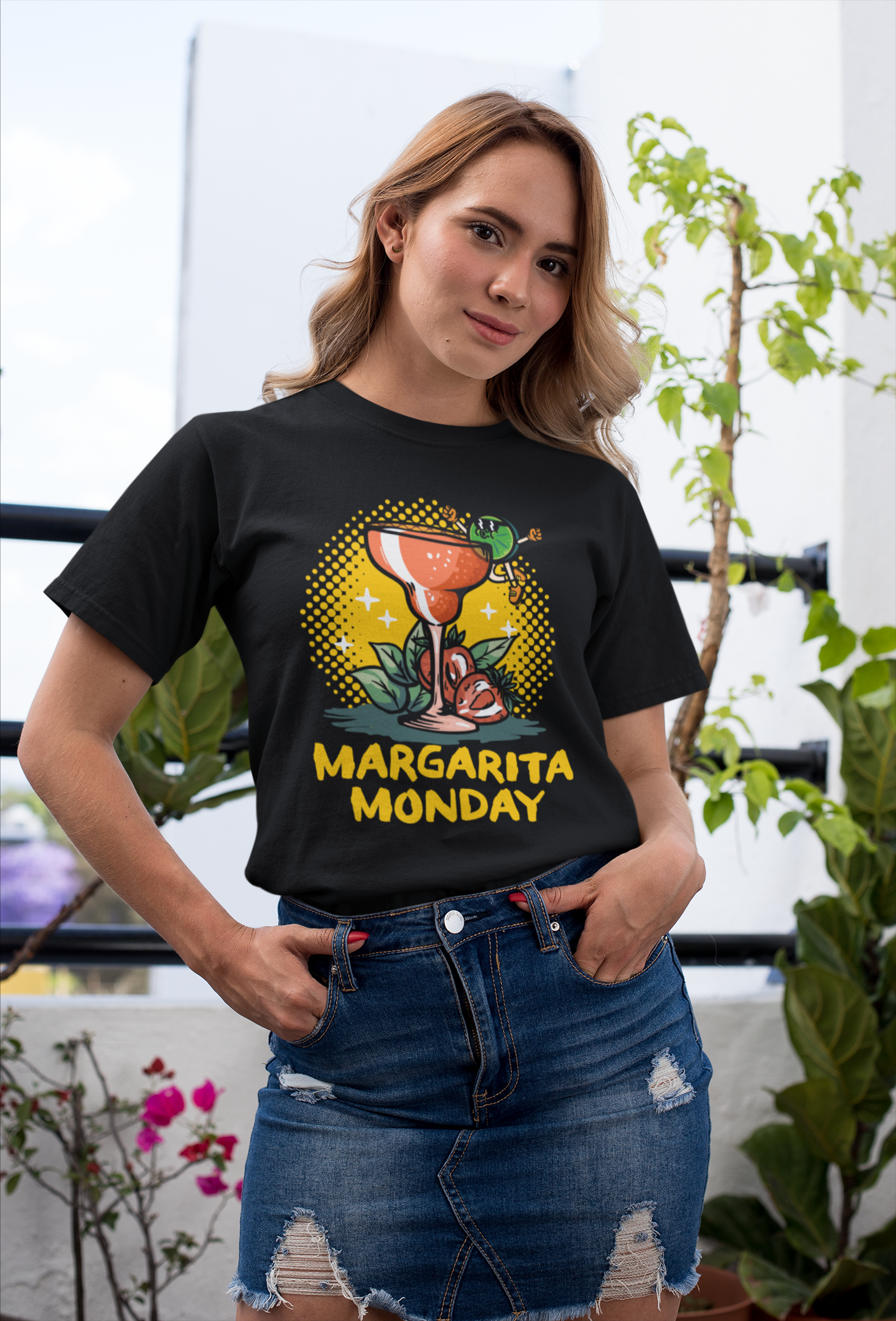 Woman wearing a black T-shirt with a "Margarita Monday" design, showcasing a vibrant margarita glass illustration with colorful accents. This stylish Margarita Monday T-shirt design adds a fun, festive touch, perfect for casual outings or celebrating Margarita Monday. The outdoor setting enhances the relaxed and cheerful vibe.