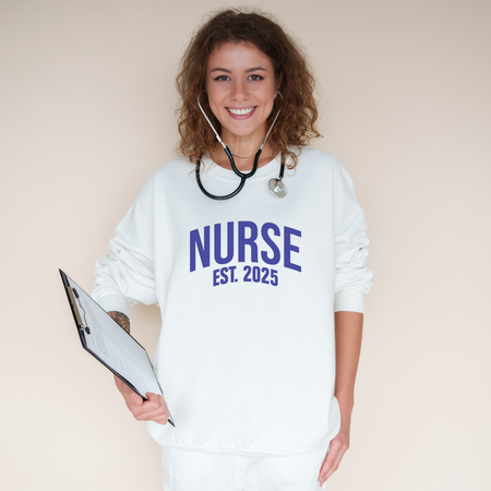 A smiling nurse wearing a "Nurse Est. 2025 Sweatshirt" in white with blue text, a stethoscope around her neck, and holding a clipboard.