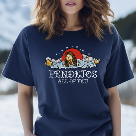 A person wearing a red t-shirt featuring an illustration of a bearded figure with open arms, holding a beer mug, surrounded by clouds and a red sun. The text "PENDEJOS ALL OF YOU" is printed below the image.