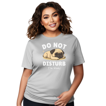 A woman wearing a gray t-shirt with a cute sleeping pug illustration and the text "DO NOT DISTURB, I'm busy" printed on it. The woman has curly hair and is smiling.