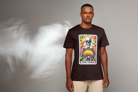 Brown T-shirt with a unique 'Taco Tuesday' design featuring a skeleton holding a large taco, surrounded by vibrant ingredients like lime slices, chili peppers, and tomatoes. Perfect for those who enjoy a fun, slightly edgy take on Taco Tuesday.