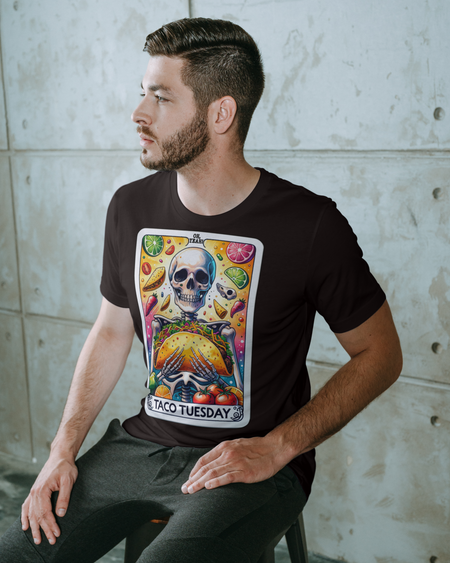 Brown T-shirt with a unique 'Taco Tuesday' design featuring a skeleton holding a large taco, surrounded by vibrant ingredients like lime slices, chili peppers, and tomatoes. Perfect for those who enjoy a fun, slightly edgy take on Taco Tuesday.